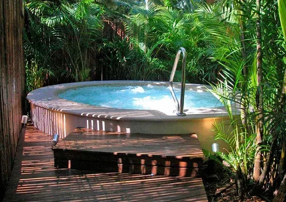In-ground concrete spa plunge pool surrounded by tropical plants, with wooden deck.