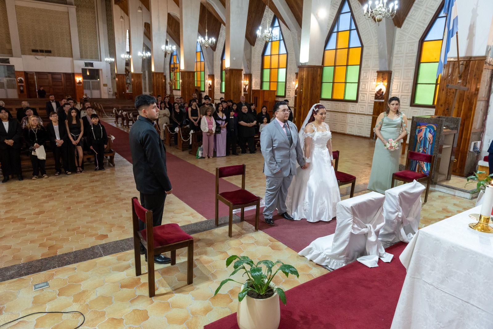 Pareja con traje de boda en el altar de una iglesia con invitados sentados en los bancos.