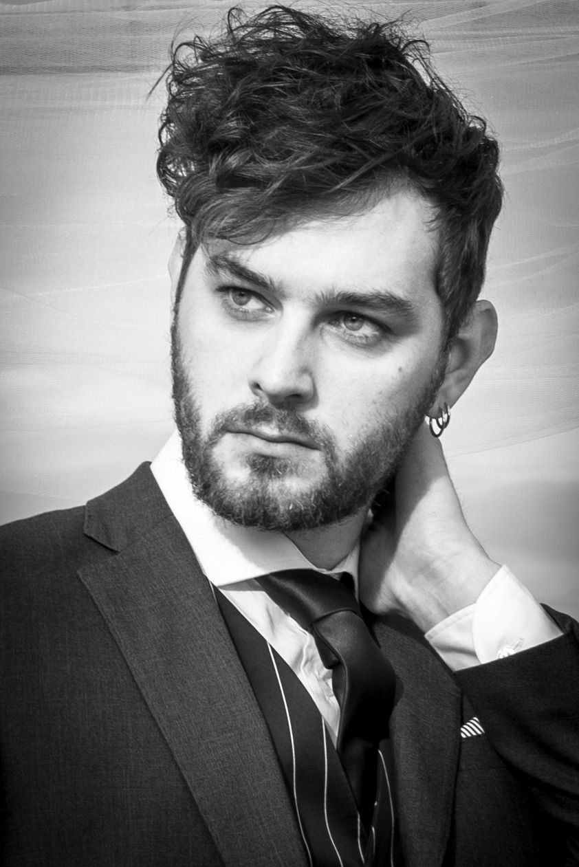 Hombre de traje, mirando hacia un lado con expresión seria, mano cerca del cuello.