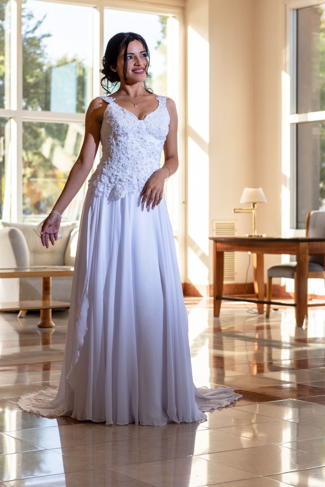Una mujer con un vestido de novia blanco sonríe en una habitación soleada.