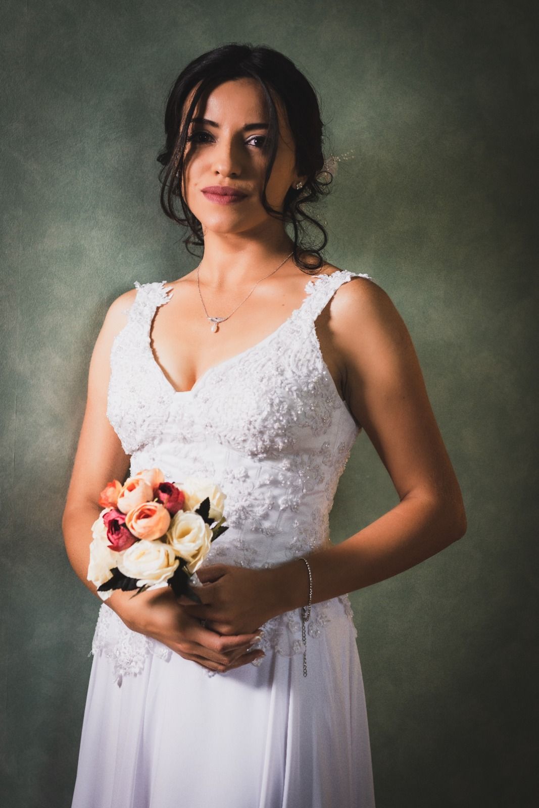 Mujer con un vestido de novia blanco sostiene un ramo, con fondo verde.