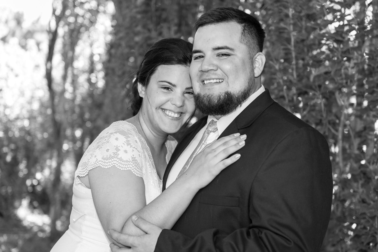 Novios abrazándose y sonriendo al aire libre. La mujer lleva un vestido de encaje; el hombre, un traje.