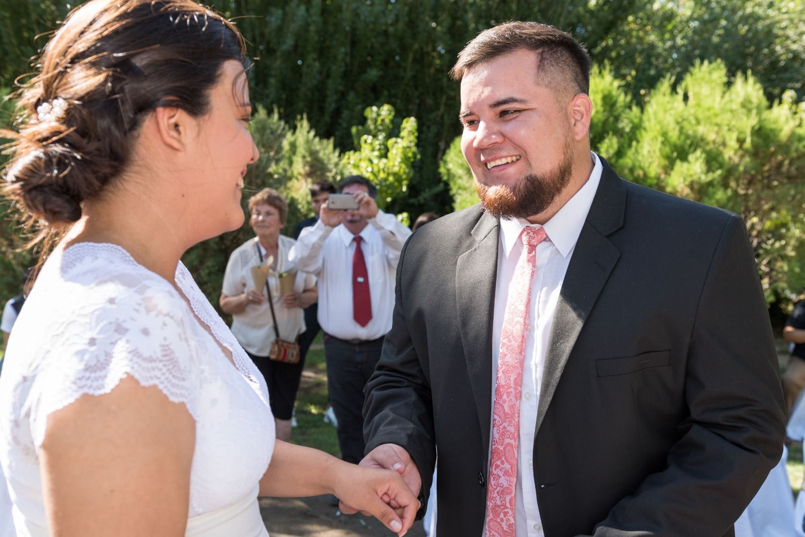 Novia y novio tomados de la mano, sonriendo, durante una ceremonia de boda al aire libre.
