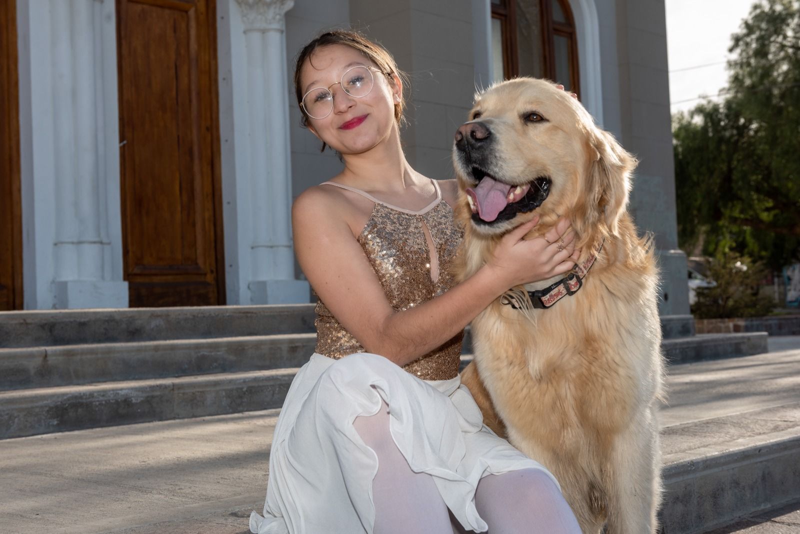Una mujer joven con atuendo de baile se sienta con un golden retriever en los escalones.