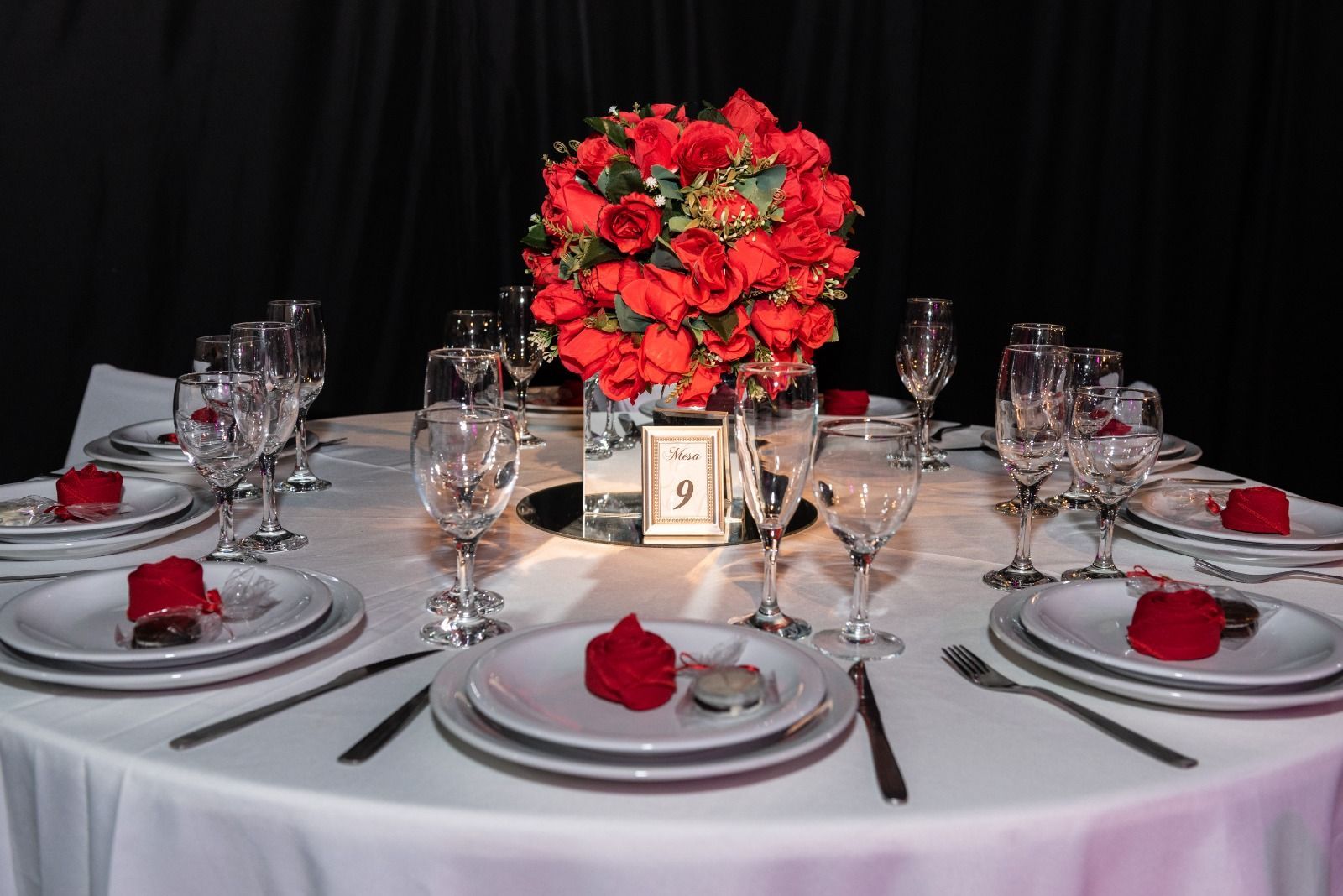 Elegante mesa con centro de rosas rojas y cubiertos para un evento formal.