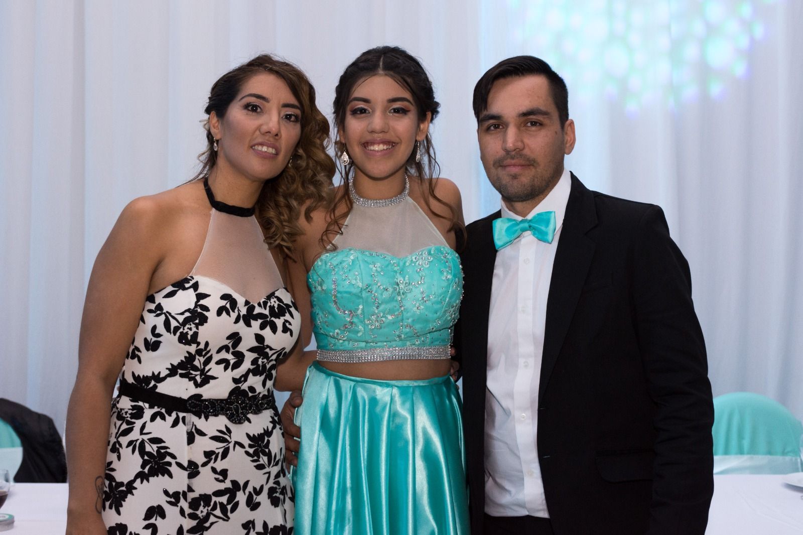 Tres personas posando en un evento: una mujer con un vestido blanco y negro