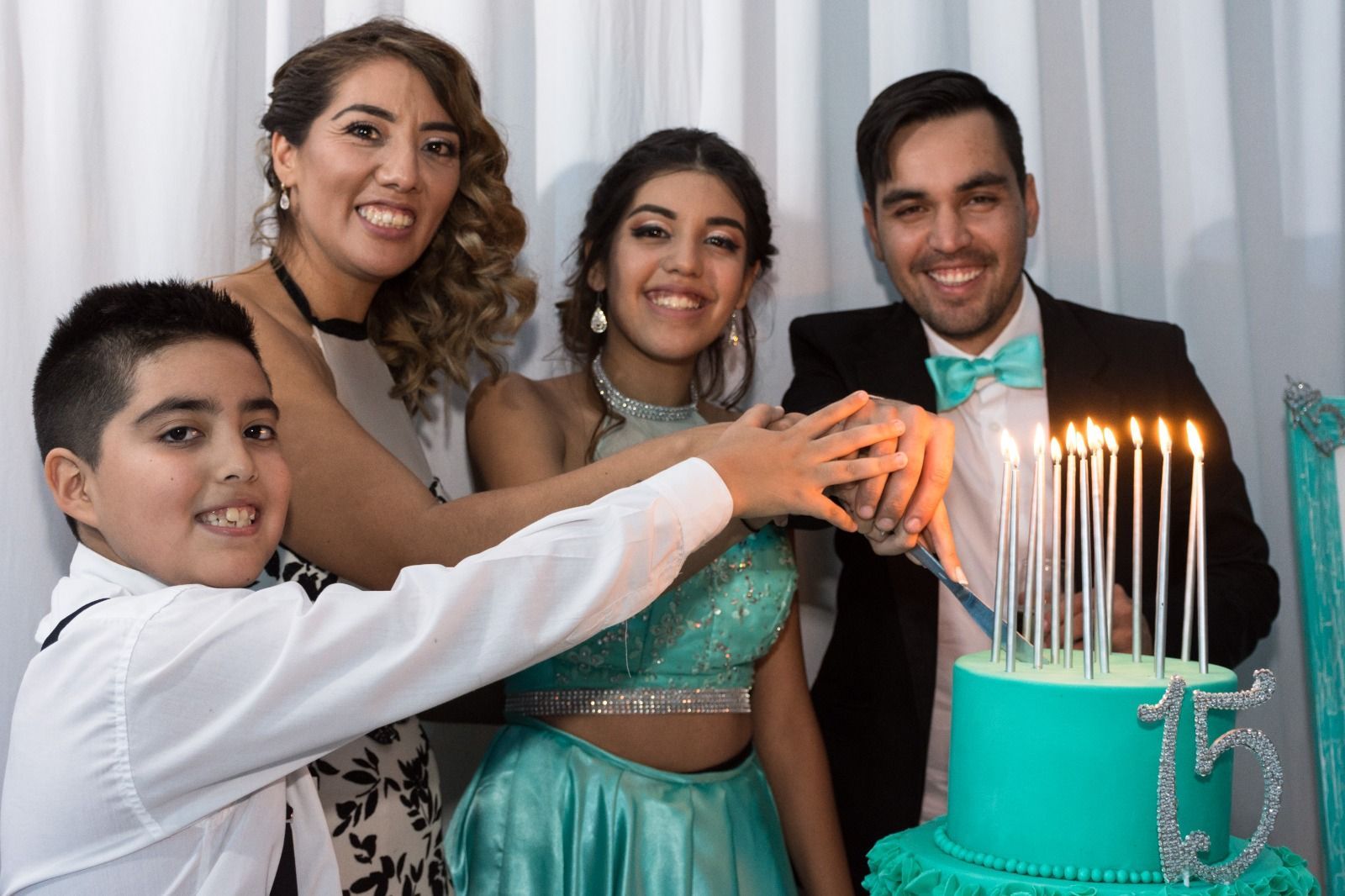 Familia encendiendo velas en un pastel glaseado color turquesa con el número 15.