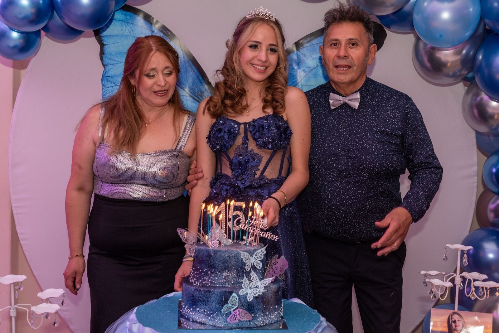 Familia celebrando junto a un pastel con temática de mariposas. 