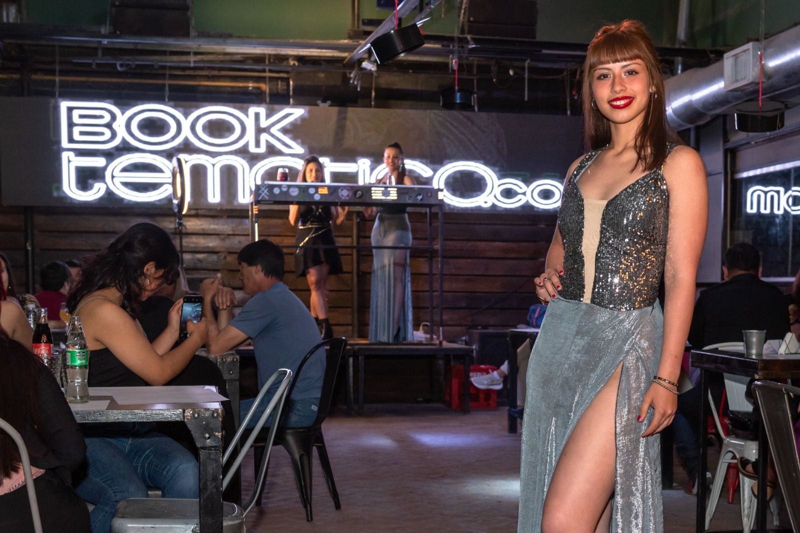Una mujer con un vestido brillante posa en un bar con música en vivo.