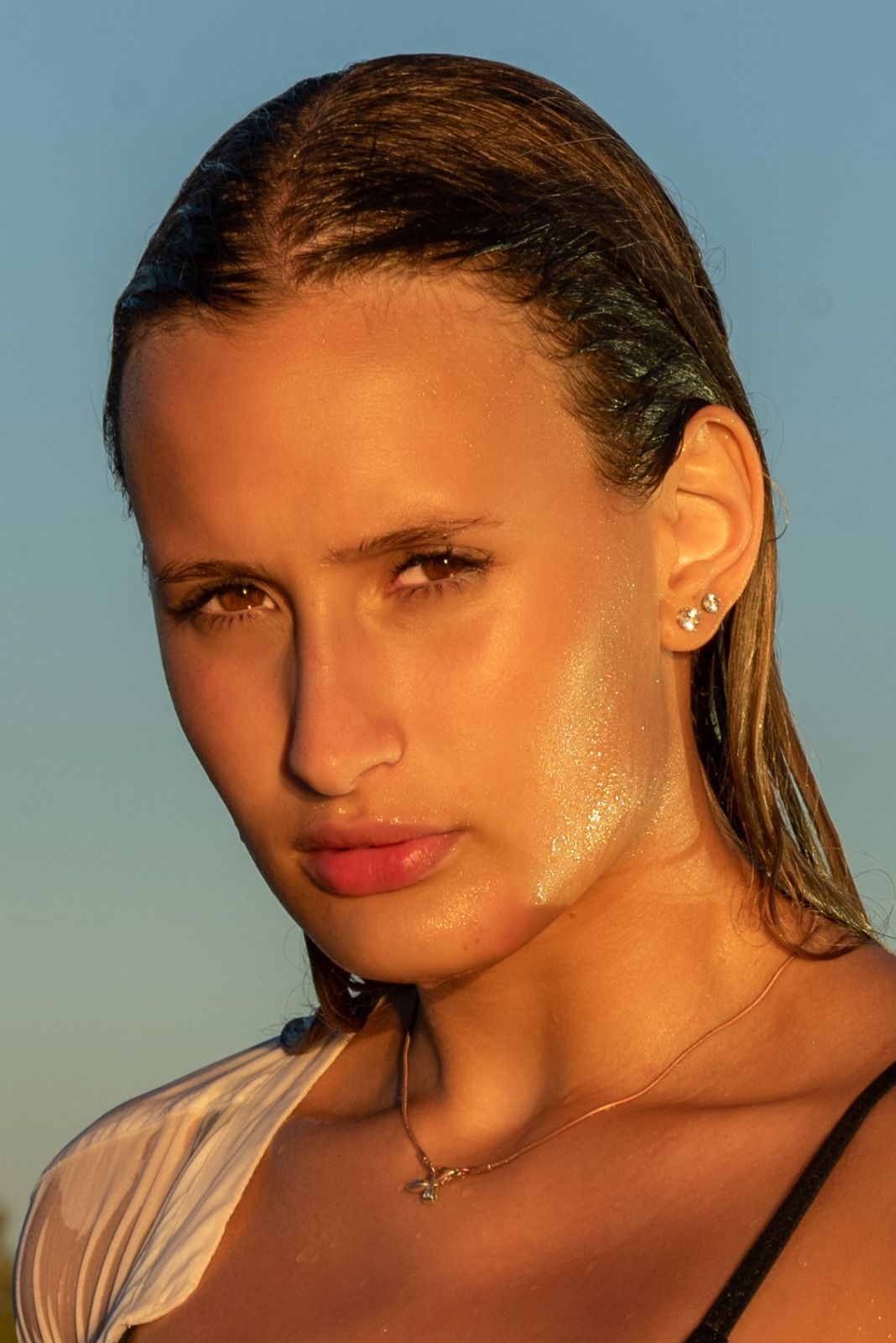 Mujer con cabello rubio mojado y peinado hacia atrás, piel iluminada por un dorado