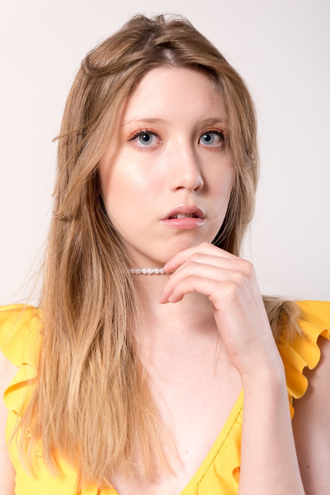 Mujer de cabello rubio, con un top amarillo, mano en la barbilla, mirando hacia adelante.
