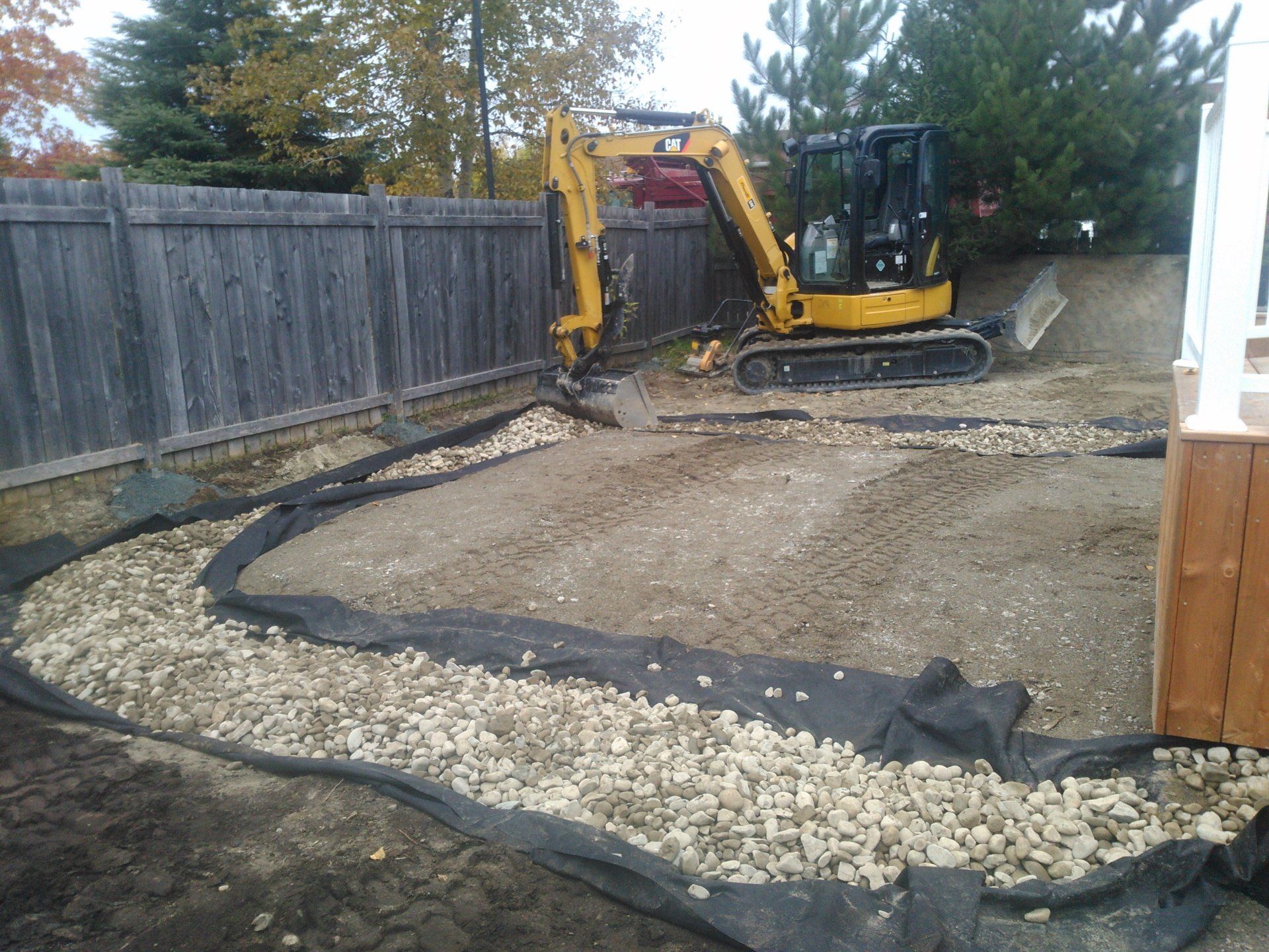 Une excavatrice jaune creuse dans une cour à côté d’une clôture en bois.