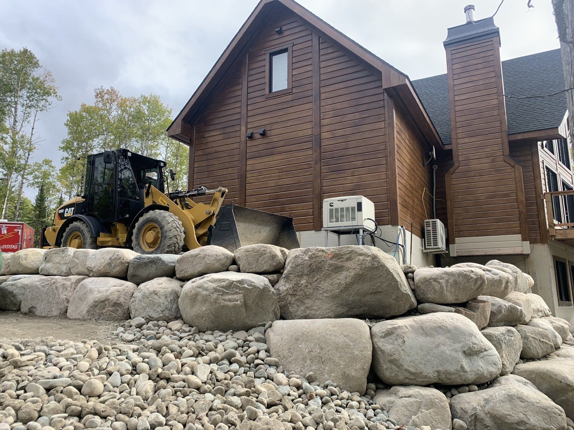 Un bulldozer est posé au sommet d’un tas de roches devant une maison.