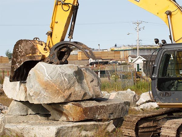Une excavatrice jaune travaille sur un gros rocher