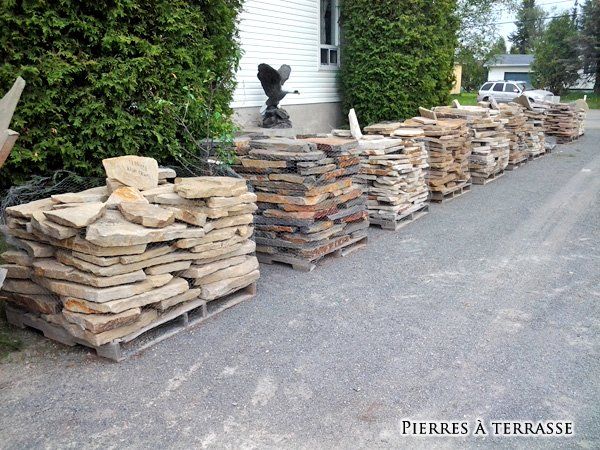 Une rangée de palettes remplies de pierres et un panneau indiquant pierres à terrasse