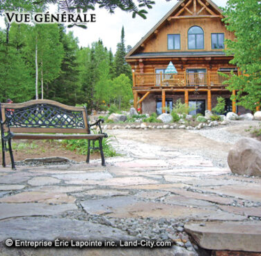 Terrasse en pierre avec banc, menant à une cabane en bois entourée d'arbres.