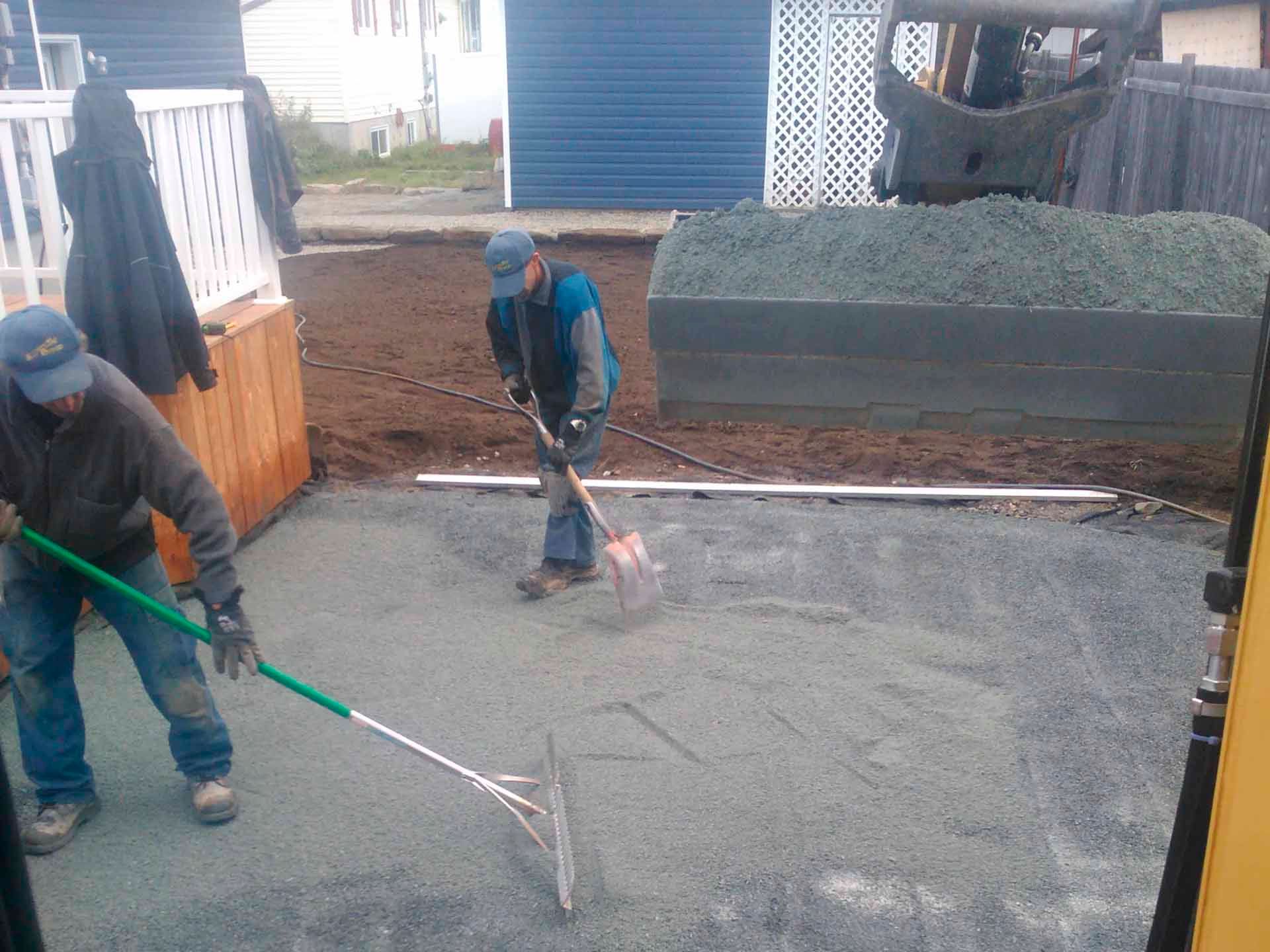 Deux hommes travaillent sur une allée en béton avec un râteau vert.
