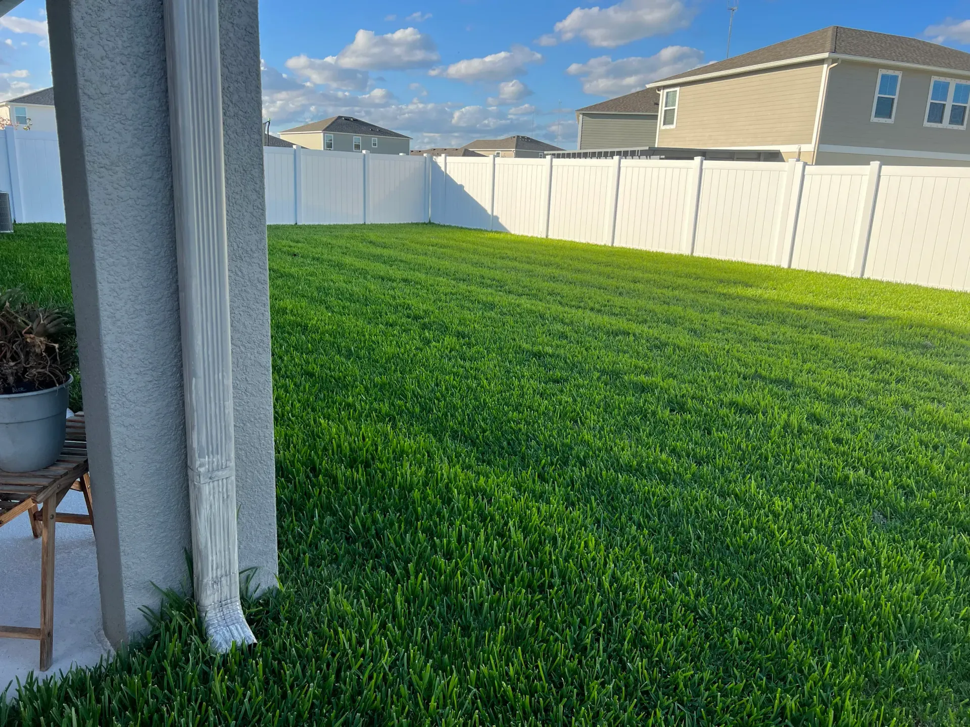 Josh Fertilizing Pro | A lush green lawn with a white fence in the backyard of a house.