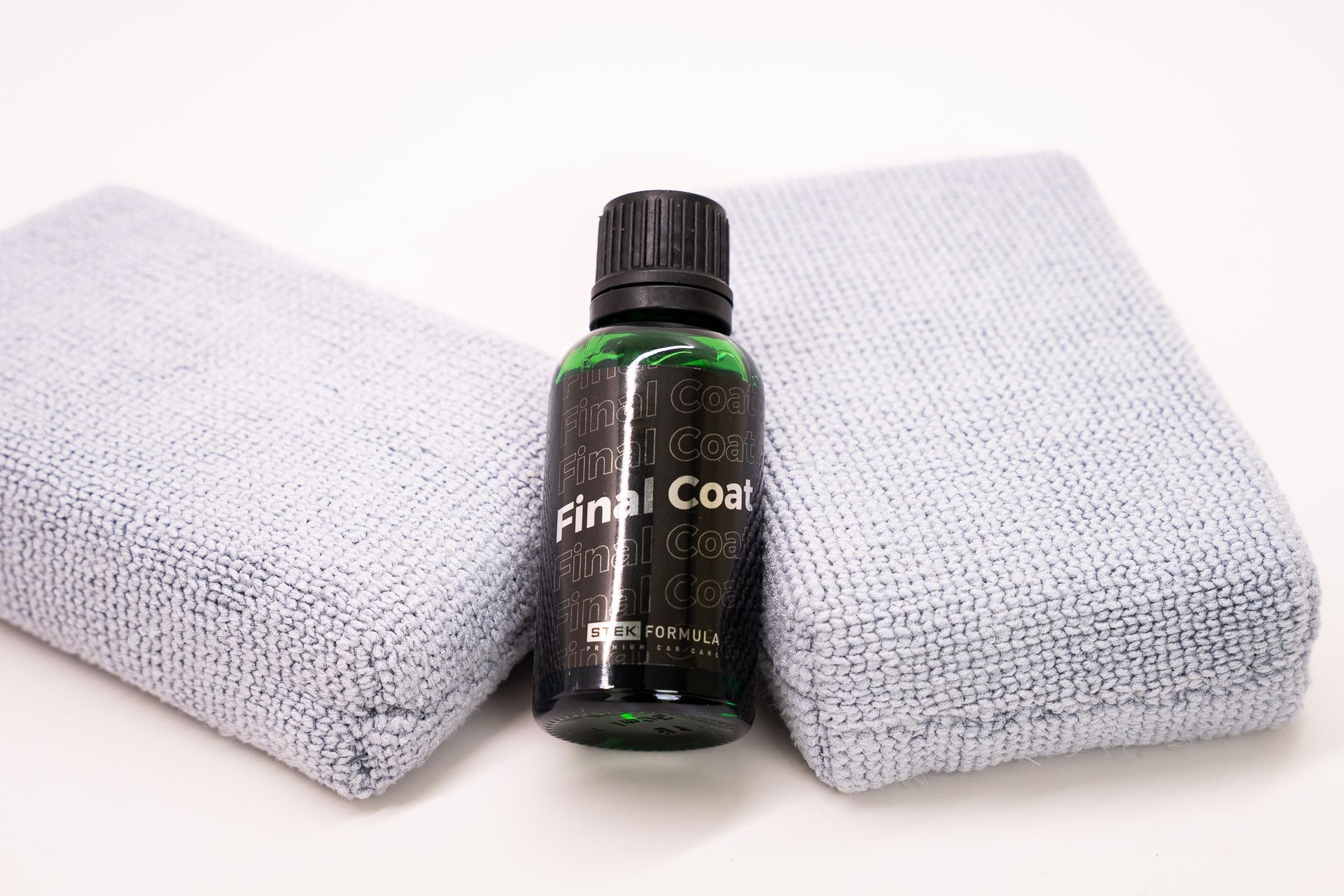 Small black bottle between two folded light gray towels on a white background