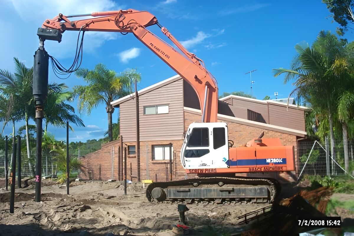 A Large Orange Excavator is in Front of a House — Q-Pile Foundations in Coolum Beach, QLD