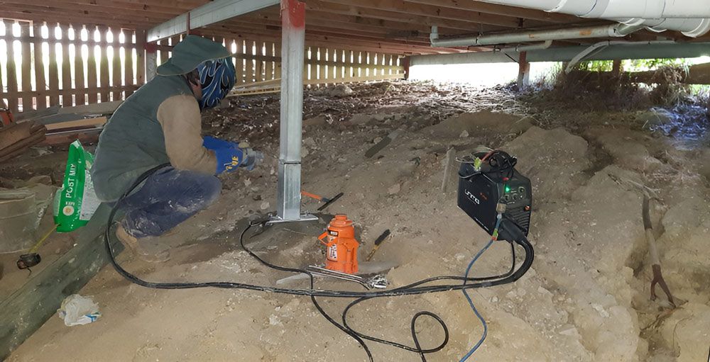 A Man is Kneeling in the Dirt Under a House — Q-Pile Foundations in Coolum Beach, QLD