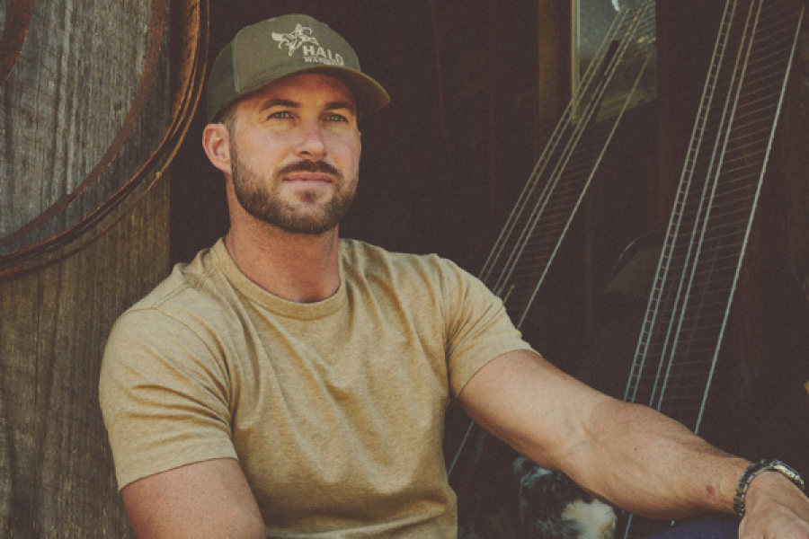 Riley Green with a beard is wearing a hat and a tan shirt.