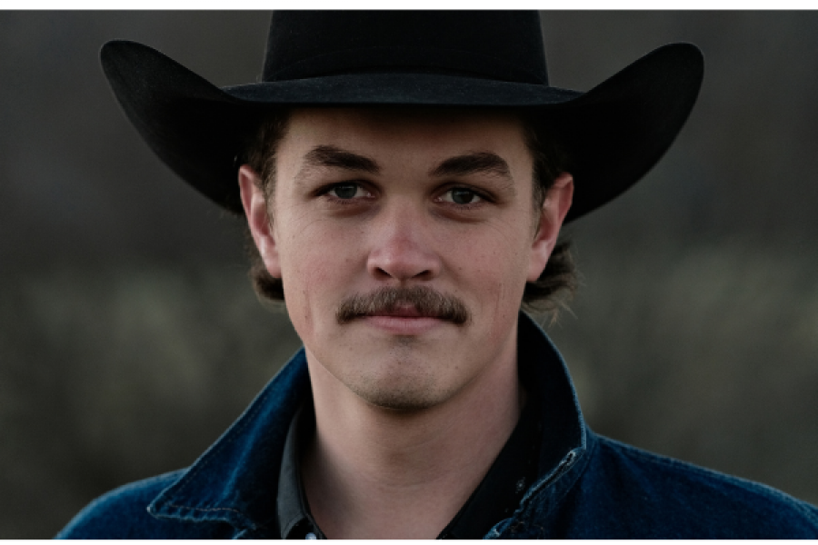 A man with a mustache is wearing a cowboy hat and a denim jacket.