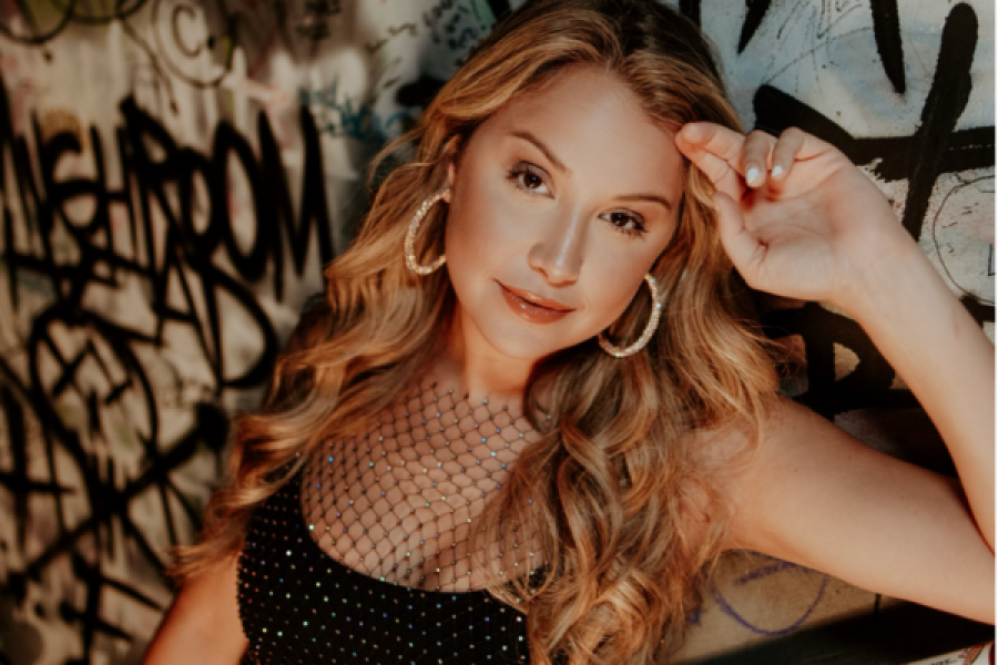 A woman wearing hoop earrings is standing in front of a graffiti wall.