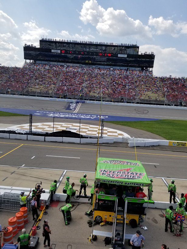 A group of people are working on a race track with a large stadium in the background