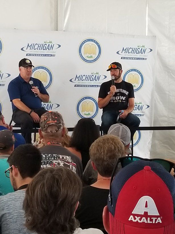 Two men are sitting on a stage talking to a crowd of people.