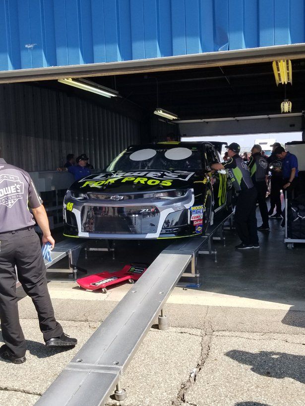 A race car is parked in a garage with people around it