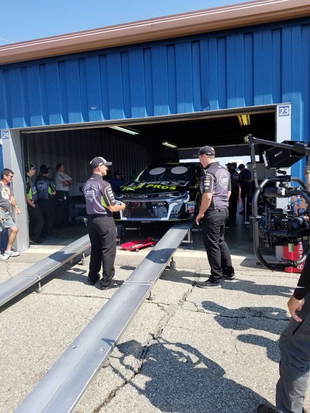 A group of men are standing in front of a car in a garage.
