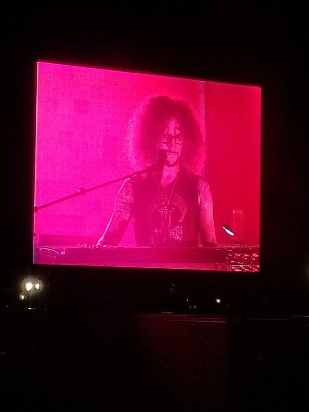 A man with curly hair is playing a keyboard and singing into a microphone.