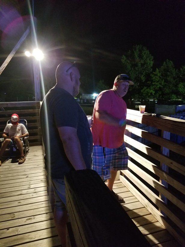 Two men are standing on a wooden deck at night.