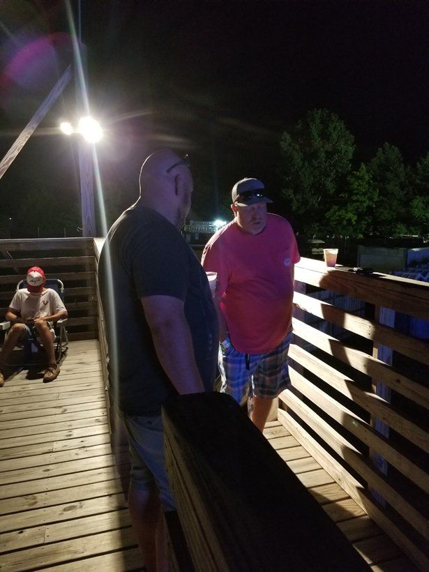 Two men are standing on a wooden bridge at night.