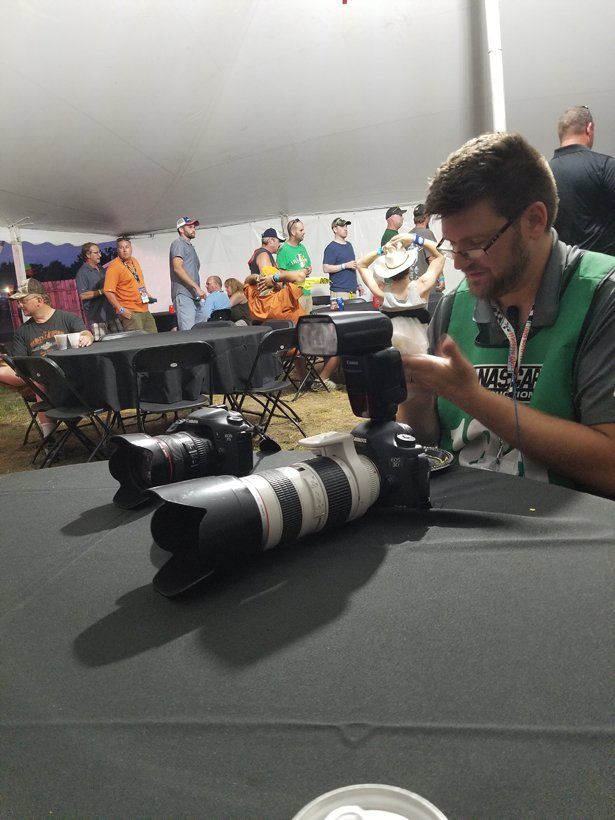 A man in a green vest is sitting at a table holding a camera.