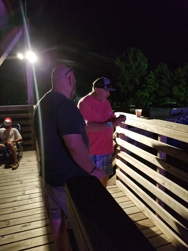 Two men are standing on a wooden deck at night.