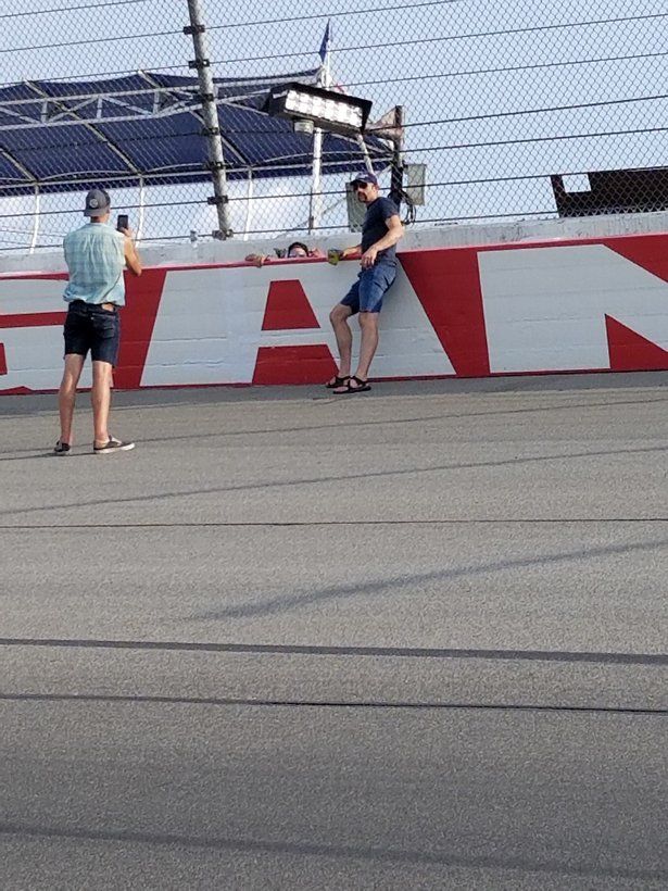 Two men are standing in front of a fan sign on a race track.