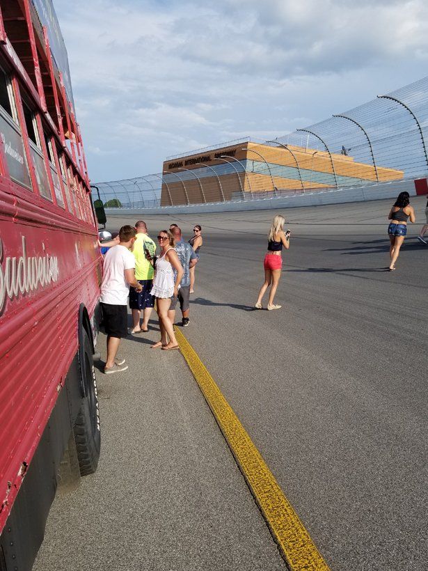 A group of people are standing in front of a red budweiser bus.