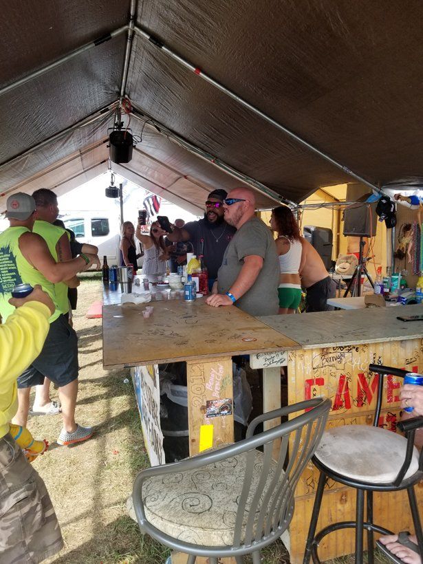 A group of people are standing around a bar under a tent.