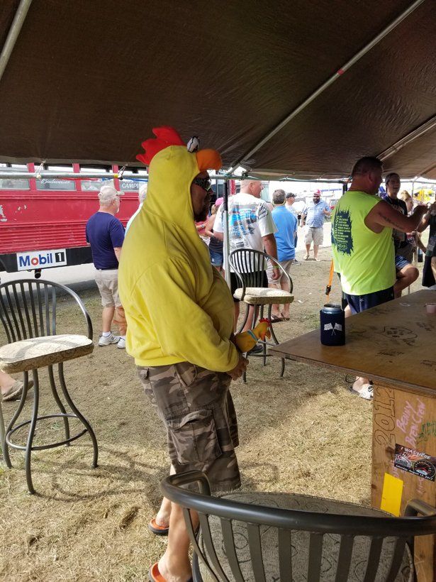 A man in a chicken costume is standing under a tent.