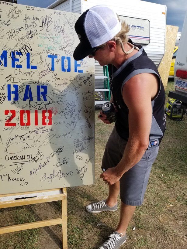 A man standing next to a sign that says mel toe har 2018