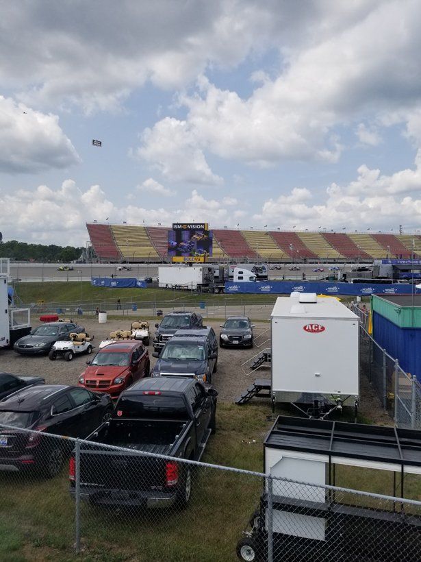 A lot of cars are parked in a lot with a stadium in the background