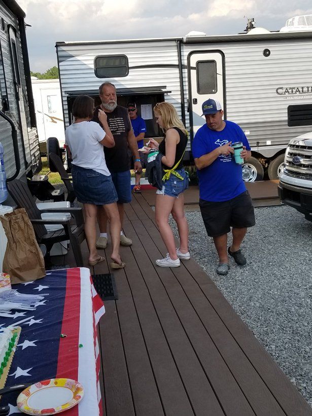 A group of people are standing on a wooden deck in front of a trailer.