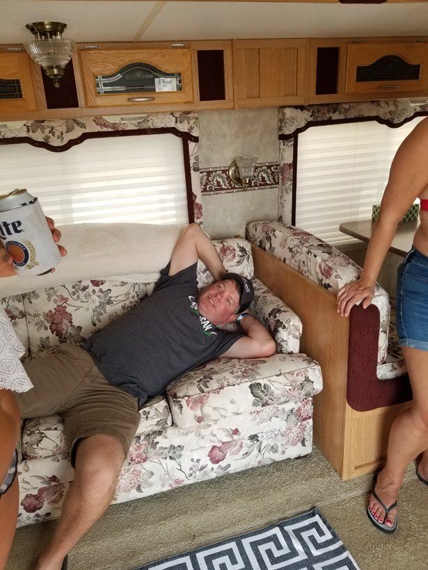 A man is laying on a couch while a woman holds a can of miller lite
