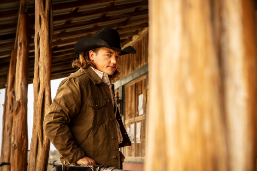 A man in a cowboy hat is standing in front of a wooden building.