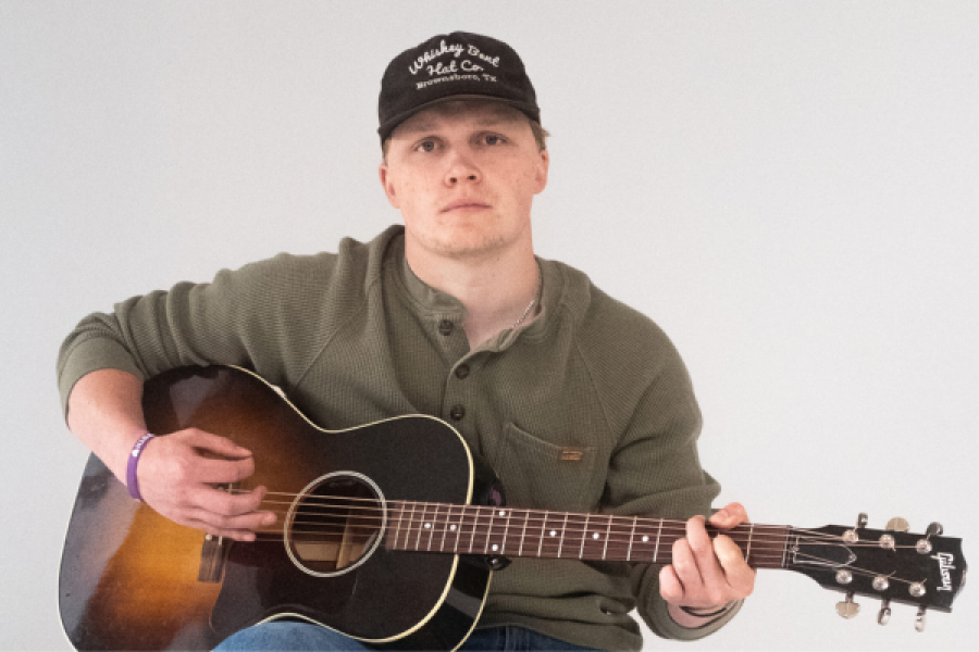 A man wearing a hat is playing an acoustic guitar.