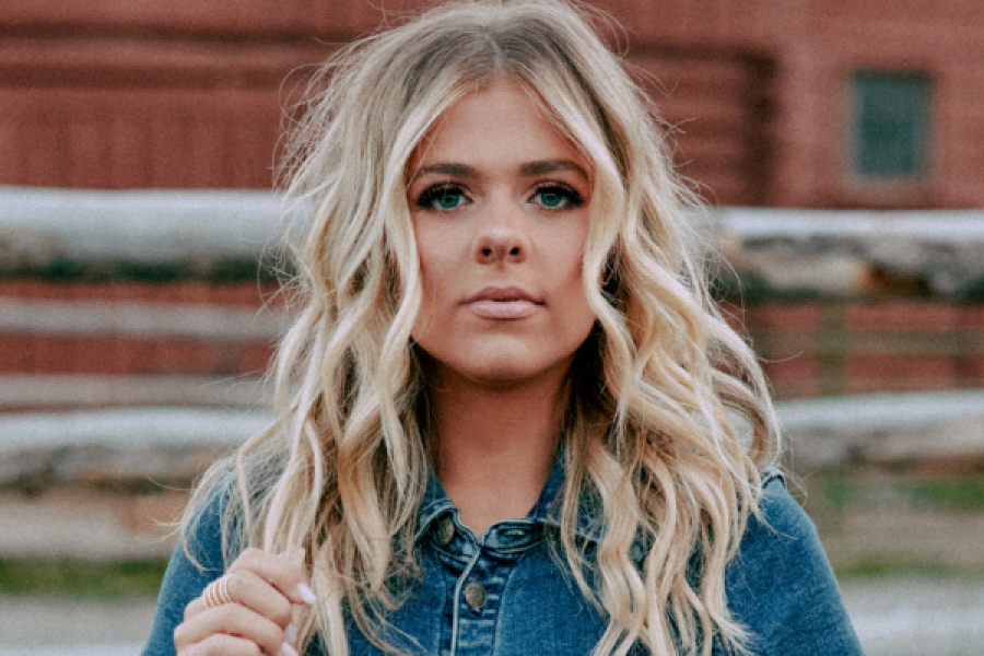 A woman in a denim shirt is standing in front of a fence.
