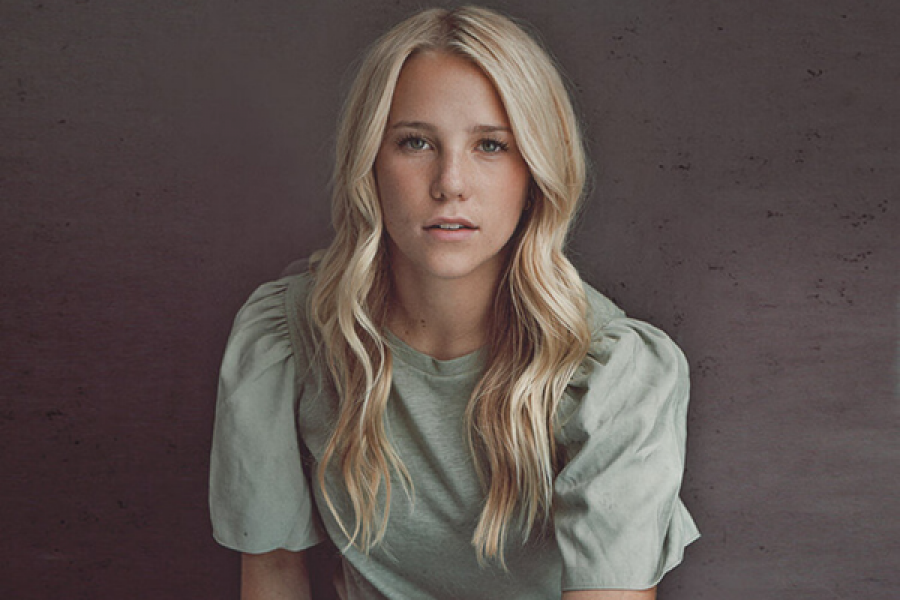 A woman with blonde hair is wearing a green shirt and looking at the camera.