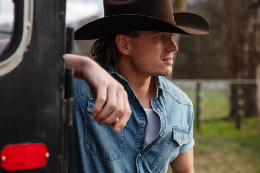 A man wearing a cowboy hat is leaning against a trailer.